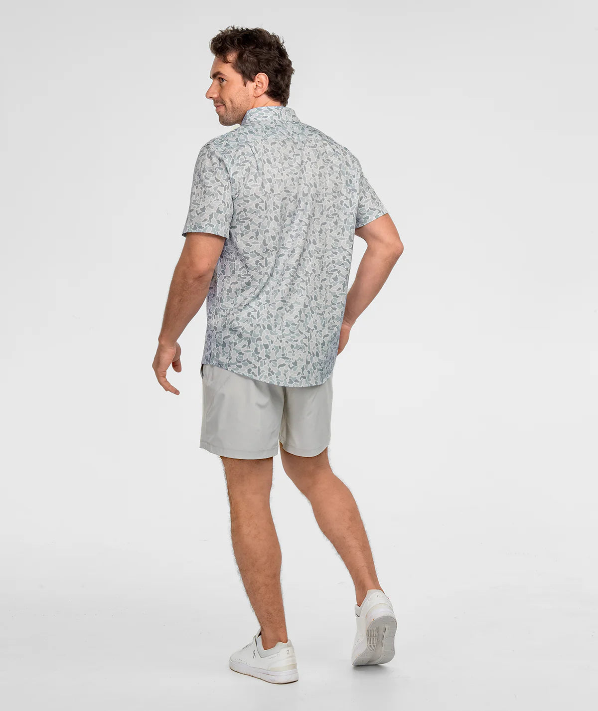 Man wearing a patterned shirt and light gray shorts on a white background